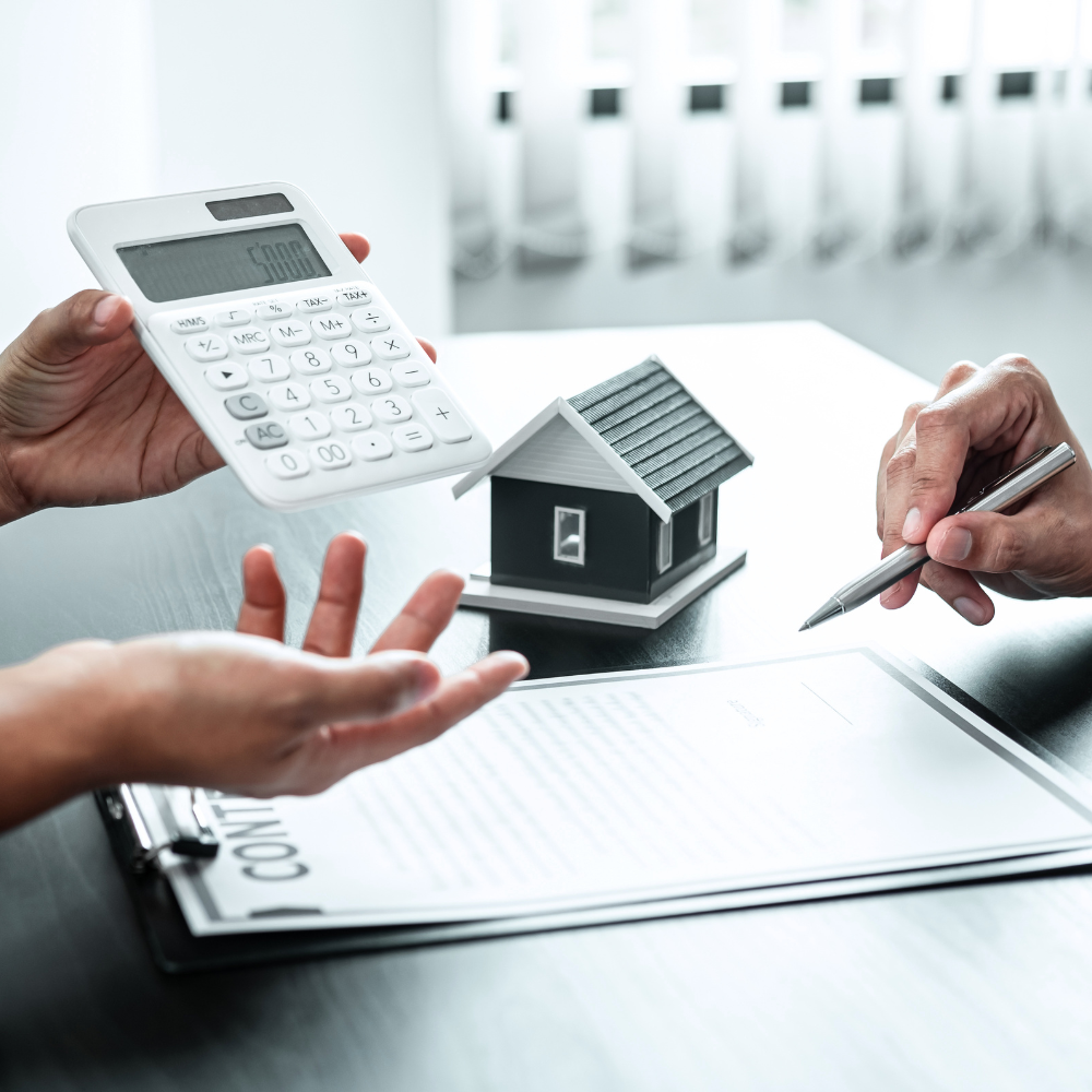 A pen poised over a loan application form for Loan Against Property, with a calculator and a model house nearby, representing property-backed lending automated by NBFCs and MFIs using Finpage's software.